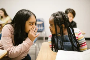Two young girls whispering in - Credits: pexels